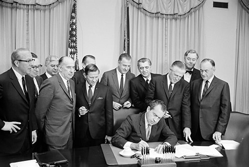 Image of President Nixon signing an Executive Order with a group of officials standing behind his desk